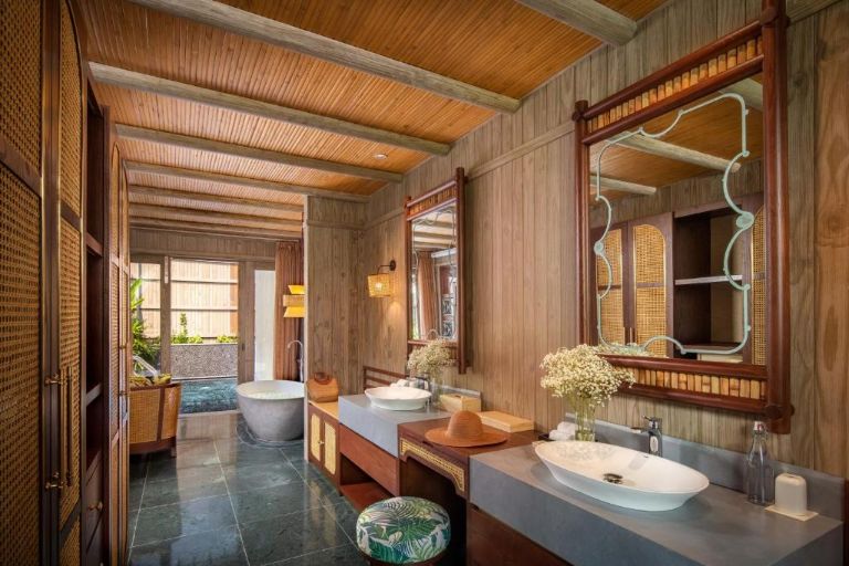 Phòng tắm riêng rộng rãi mang sắc nâu chủ đạo từ gỗ và được tạo điểm nhấn bằng chiếc ghế tròn bọc vải tropical. (Nguồn: internet)