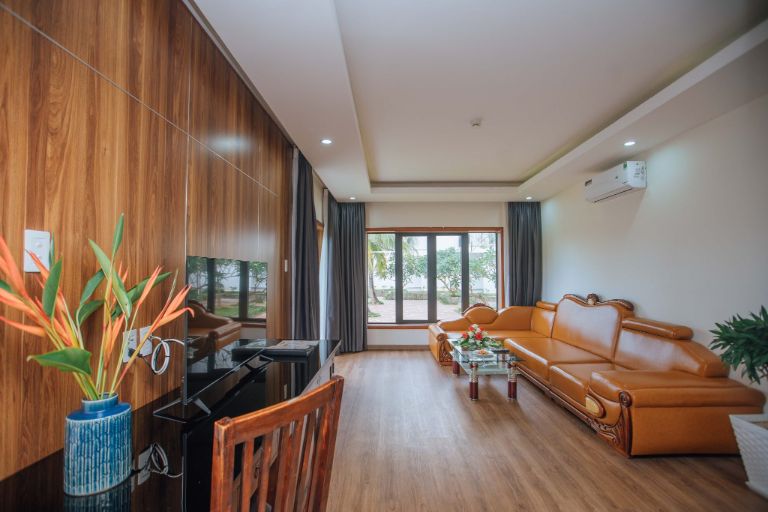 Phòng khách của phòng Suite Hướng Bể Bơi có thiết kế hiện đại khi nội thất chủ yếu được làm từ gỗ, bộ sofa cao cấp màu nâu bò to lớn và êm ái khiến không gian càng thêm phần sang trọng.