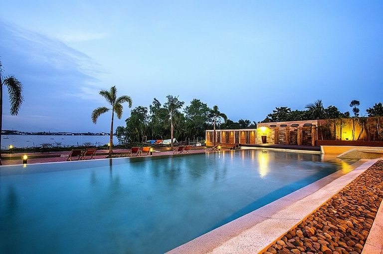 Mekong Rustic Resort với hồ bơi lộ thiên thiết kế hình lười liềm ấn tượng. Bên hồ là rặng cây xanh và ghế tắm nắng đan bằng tre thủ công. 