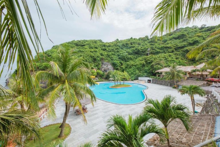 Cát Bà Island Hotel với bể bơi được thiết kế uốn lượn, bao quanh là những rặng dừa cao và hệ thống ghế tắm, ô che. 